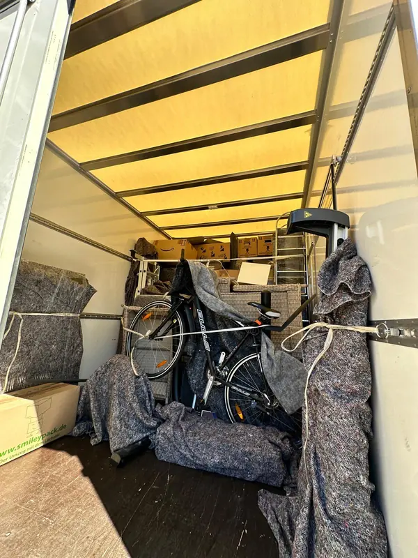 Fahrrad und Möbel mit Spanngurten und Decken im Umzugswagen gesichert